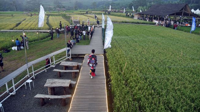 Seorang model mengenakan busana dari bahan kain perca saat peragaan busana di tengah persawahan di kampung tematik Agro Eduwisata Organik Mulyaharja, Kota Bogor, Jawa Barat, Selasa (5/7/2022).  ANTARA FOTO/Arif Firmansyah
