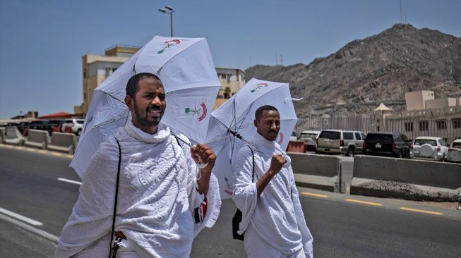 Jamaah haji berjalan dengan payung di Mina dekat kota suci Makkah, Arab Saudi, Kamis (7/7/2022). [Delil SOULEIMAN / AFP]