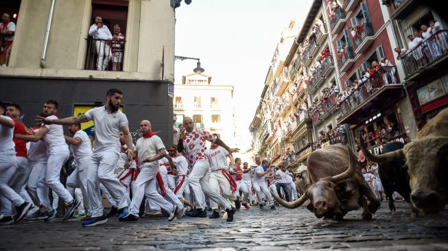 Para peserta berlari di depan banteng selama acara "encierro" (lari banteng) saat festival San Fermin di Pamplona, Spanyol, Kamis (7/7/2022). [MIGUEL RIOPA / AFP]
