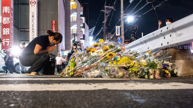 Seorang warga menaruh bunga dan berdoa untuk mantan Perdana Menteri Jepang Abe Shinzo di TKP penembakan di luar Stasiun Yamato Saidaiji di Nara, Jepang, Jumat (8/7/2022). [Philip FONG / AFP]
