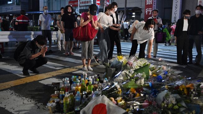 Warga menaruh bunga dan berdoa untuk mantan Perdana Menteri Jepang Abe Shinzo di TKP penembakan di luar Stasiun Yamato Saidaiji di Nara, Jepang, Jumat (8/7/2022). [Philip FONG / AFP]
