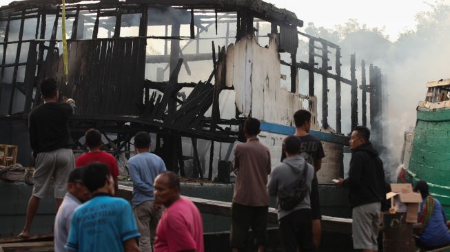 Warga mengamati bangkai kapal kargo yang terbakar di Pelabuhan Kalimas Surabaya, Jawa Timur, Minggu (17/7/2022). [ANTARA FOTO/Didik Suhartono/aww]