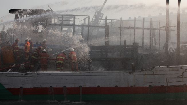 Petugas Dinas Pemadam Kebakaran Kota Surabaya melakukan proses pembasahan kapal kargo yang terbakar di Pelabuhan Kalimas Surabaya, Jawa Timur, Minggu (17/7/2022). [ANTARA FOTO/Didik Suhartono/aww]