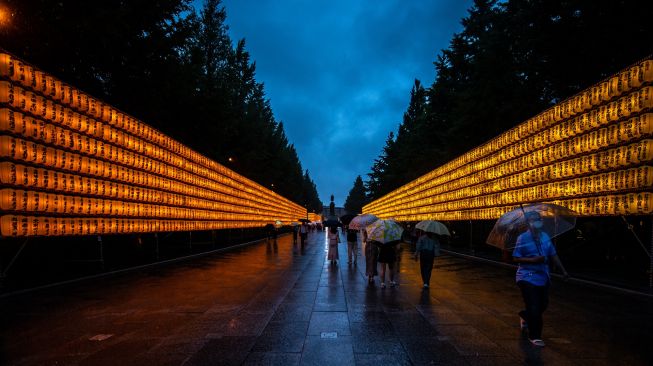 Orang-orang berjalan di antara lentera yang menyala saat festival Mitama Matsuri di Kuil Yasukuni, Tokyo, Jepang, Kamis (14/7/2022). [Philip FONG / AFP]
