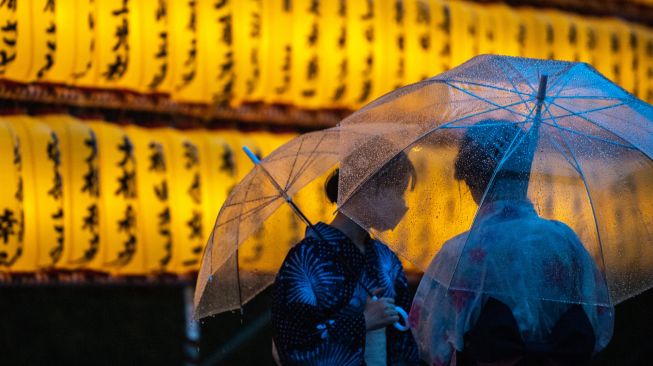 Wanita mengenakan pakaian tradisional berswafoto dengan latar belakang lentera yang menyala saat festival Mitama Matsuri di Kuil Yasukuni, Tokyo, Jepang, Kamis (14/7/2022). [Philip FONG / AFP]