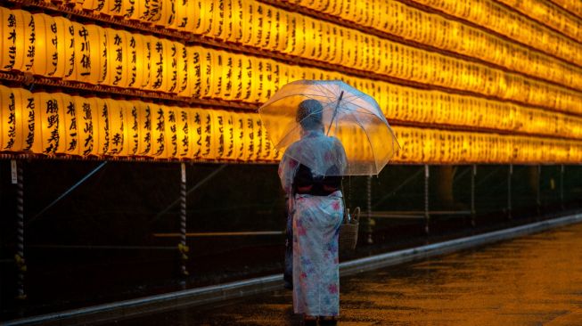 Wanita mengenakan pakaian tradisional berswafoto dengan latar belakang lentera yang menyala saat festival Mitama Matsuri di Kuil Yasukuni, Tokyo, Jepang, Kamis (14/7/2022). [Philip FONG / AFP]