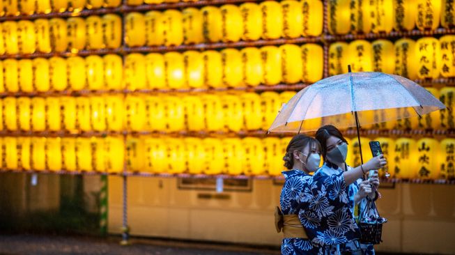 Wanita mengenakan pakaian tradisional berswafoto dengan latar belakang lentera yang menyala saat festival Mitama Matsuri di Kuil Yasukuni, Tokyo, Jepang, Kamis (14/7/2022). [Philip FONG / AFP]