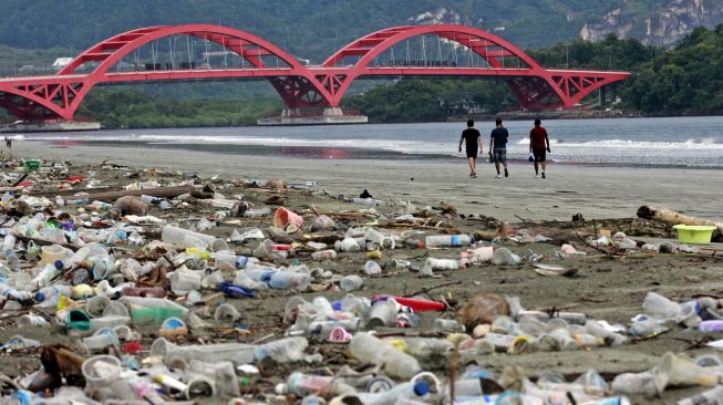 Sejumlah warga melintas di dekat sampah-sampah plastik di pesisir Teluk Youtefa, Jayapura, Papua, Sabtu (23/7/2022).  ANTARA FOTO/Gusti Tanati
