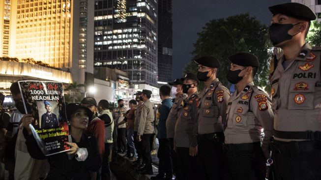 Peserta aksi dari Tim Advokat Penegakan Hukum dan Keadilan (TAMPAK) menunjukan poster Alm Brigadir Yosua Hutabarat kepada anggota polisi saat aksi seribu lilin dan doa bersama di Bundaran HI, Jakarta, Jumat (22/7/2022).  ANTARA FOTO/Muhammad Adimaja
