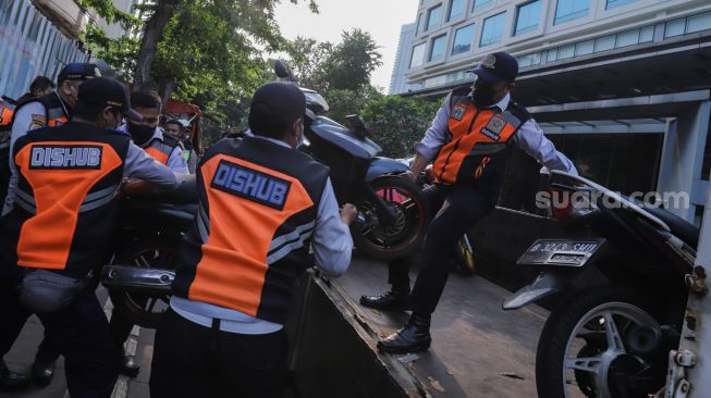 Petugas mengangkut sepeda motor yang parkir liar ke atas truk di lokasi Citayam Fashion Week di kawasan Dukuh Atas, Jakarta Pusat, Selasa (26/7/2022). [Suara.com/Alfian Winanto]