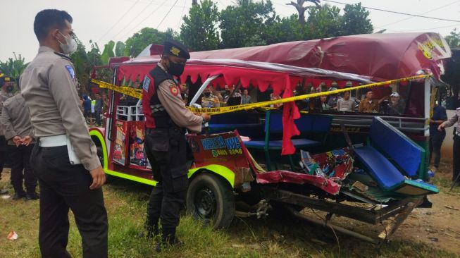 Polisi memasang police line di odong-odong tertabrak Kereta Api Merak-Rangkasbitung di Kragilan, Serang, Banten, Selasa (26/7/2022). [Anwar/Suara.com]