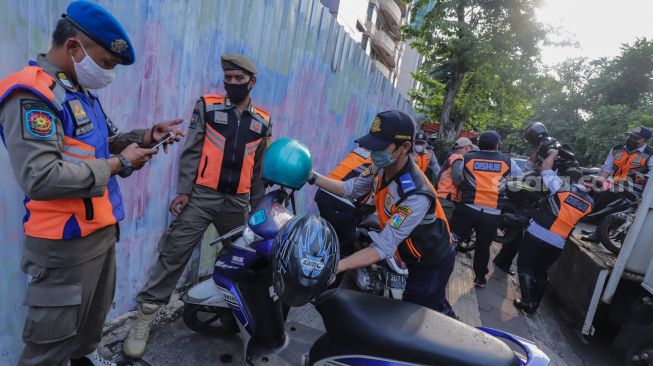 Petugas mengangkut sepeda motor yang parkir liar ke atas truk di lokasi Citayam Fashion Week di kawasan Dukuh Atas, Jakarta Pusat, Selasa (26/7/2022). [Suara.com/Alfian Winanto]