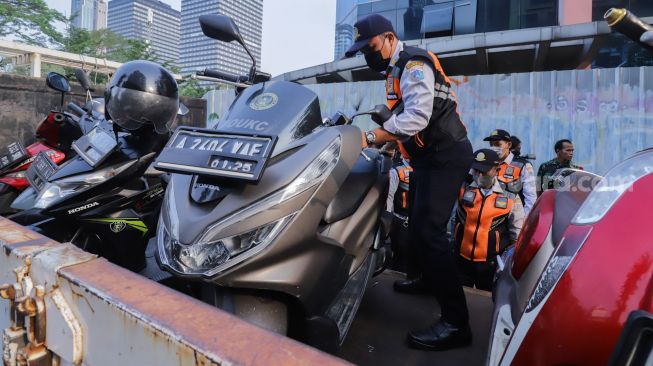 Petugas mengangkut sepeda motor yang parkir liar ke atas truk di lokasi Citayam Fashion Week di kawasan Dukuh Atas, Jakarta Pusat, Selasa (26/7/2022). [Suara.com/Alfian Winanto]