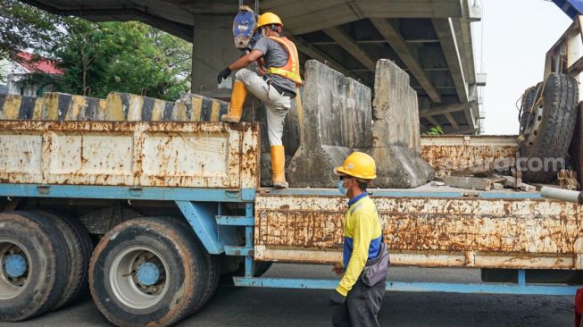 Petugas Dinas Perhubungan (Dishub) DKI Jakarta menurunkan beton pembatas jalan untuk menutup Jembatan Kapin di Duren Sawit, Jakarta Timur, Kamis (28/7/2022). [Suara.com/Alfian Winanto]