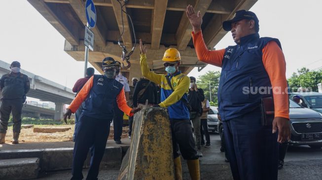 Petugas Dinas Perhubungan (Dishub) DKI Jakarta menurunkan beton pembatas jalan untuk menutup Jembatan Kapin di Duren Sawit, Jakarta Timur, Kamis (28/7/2022). [Suara.com/Alfian Winanto]