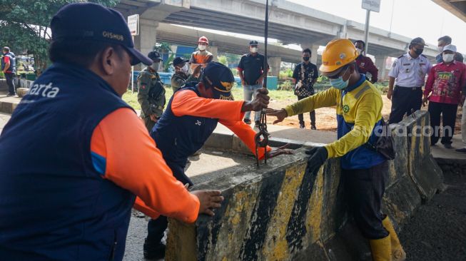 Petugas Dinas Perhubungan (Dishub) DKI Jakarta menurunkan beton pembatas jalan untuk menutup Jembatan Kapin di Duren Sawit, Jakarta Timur, Kamis (28/7/2022). [Suara.com/Alfian Winanto]