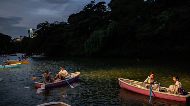 Orang-orang berlayar dengan perahu dayung saat festival lentera terapung di Chidorigafuchi, Tokyo, Jepang, Jumat (29/7/2022). [Philip FONG / AFP]