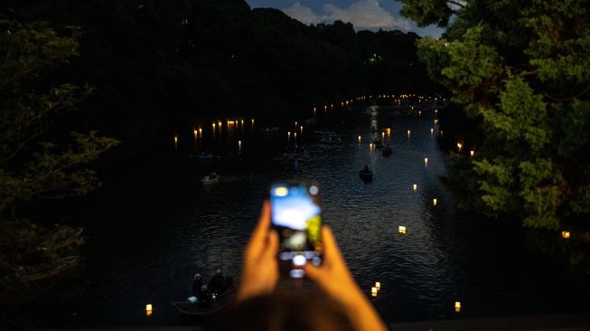 Pengunjung mengambil gambar saat orang-orang mengarungi perahu dayung selama festival lentera terapung di Chidorigafuchi, Tokyo, Jepang, Jumat (29/7/2022). [Philip FONG / AFP]
