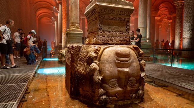 Orang-orang melihat patung kepala medusa saat mengunjungi situs bersejarah Basilica Cistern di Istanbul, Turki, Selasa (26/7/2022). [Yasin AKGUL/AFP]