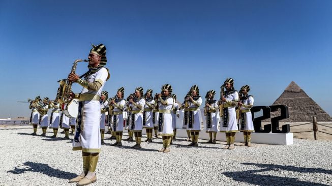 Anggota marching band yang mengenakan pakaian Mesir kuno tampil dsaat acara Pyramids Air Show 2022 di dataran tinggi Piramida Giza, Mesir, Rabu (3/8/2022). [Mahmoud Khaled / AFP]
