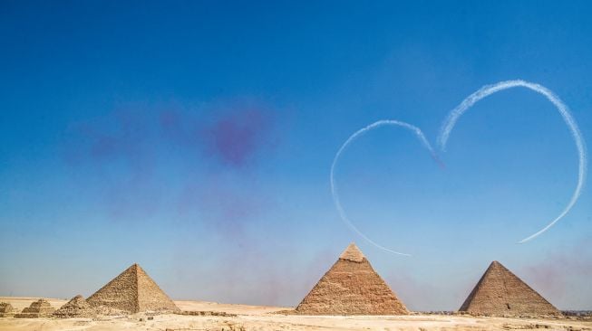 Pesawat K-8E Karakorum dari tim aerobatik Angkatan Udara Mesir 'Silver Stars' bermanuver saat acara Pyramids Air Show 2022 di dataran tinggi Piramida Giza, Mesir, Rabu (3/8/2022). [Mahmoud Khaled / AFP]
