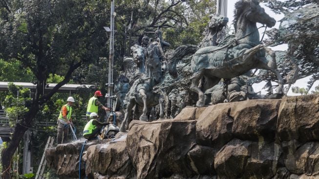 Pekerja membersihkan patung Arjuna Wijaya atau yang lebih dikenal sebagai patung kuda di jalan Medan Merdeka Barat, Jakarta Barat, Selasa (9/8/2022). [Suara.com/Alfian Winanto]