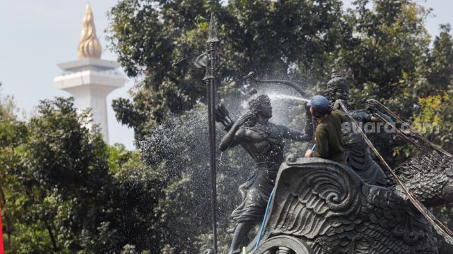 Pekerja membersihkan patung Arjuna Wijaya atau yang lebih dikenal sebagai patung kuda di jalan Medan Merdeka Barat, Jakarta Barat, Selasa (9/8/2022). [Suara.com/Alfian Winanto]