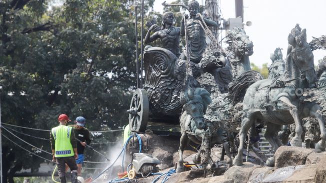 Pekerja membersihkan patung Arjuna Wijaya atau yang lebih dikenal sebagai patung kuda di jalan Medan Merdeka Barat, Jakarta Barat, Selasa (9/8/2022). [Suara.com/Alfian Winanto]