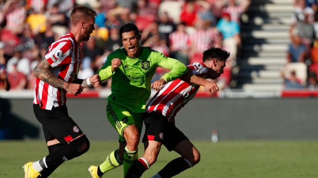 Striker Manchester United Cristiano Ronaldo (tengah) dilanggar oleh bek Brentford Aaron Hickey (kanan) saat pertandingan sepak bola Liga Premier Inggris antara Brentford dan Manchester United di Stadion Brentford Community, London, Inggris, Sabtu (13/8/2022). [Ian Kington / AFP]