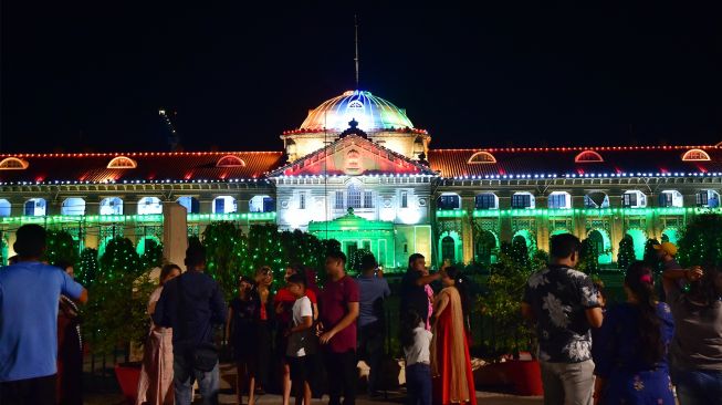 Orang-orang berfoto di depan Pengadilan Tinggi Allahabad yang menyala dengan warna bendera nasional India di Allahabad, India, Sabtu (13/8/2022). [SANJAY KANOJIA / AFP]
