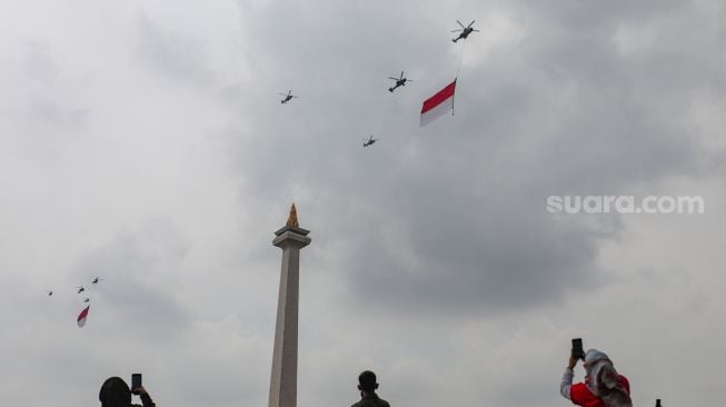 Helikopter gabungan milik TNI-Polri terbang melintas dengan bendera merah putih raksasa di atas Monas saat Peringatan Detik-Detik Proklamasi di Perpustakaan Nasional, Jakarta Pusat, Rabu (17/8/2022). [Suara.com/Alfian Winanto]