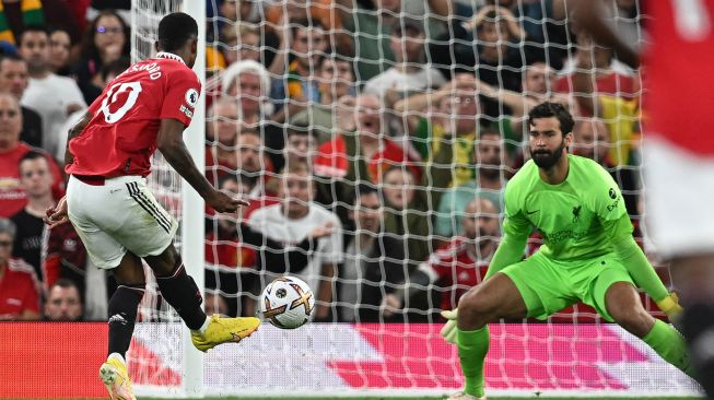 Striker Manchester United Marcus Rashford (kiri) menembak melewati kiper Liverpool Alisson Becker (kanan) untuk mencetak gol kedua mereka selama pertandingan sepak bola Liga Premier Inggris antara Manchester United melawan Liverpool di Old Trafford, Selasa (23/8/2022) dini hari WIB.
 Paul ELLIS / AFP