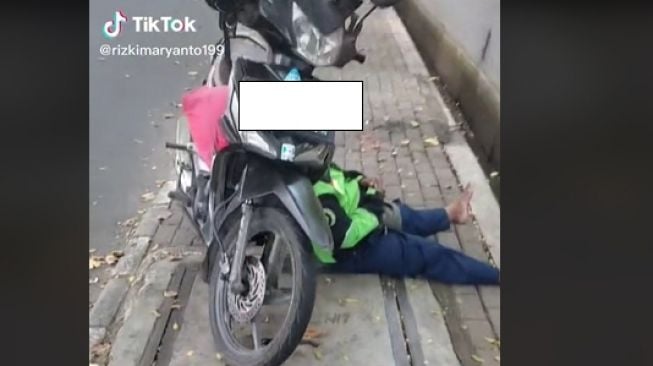 Ojol tertidur di trotoar dengan memanfaatkan motor sebagai bantal (TikTok)