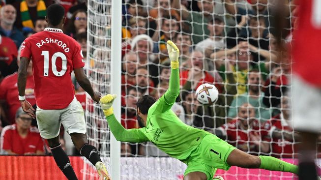 Striker Manchester United Marcus Rashford (kiri) menembak melewati kiper Liverpool Alisson Becker (kanan) untuk mencetak gol kedua mereka selama pertandingan sepak bola Liga Premier Inggris antara Manchester United melawan Liverpool di Old Trafford, Selasa (23/8/2022) dini hari WIB.
 Paul ELLIS / AFP