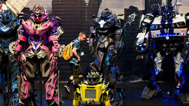 Pengunjung berdiri di antara figur transformer saat pameran video game Gamescom di Cologne, Jerman, Rabu (24/8/2022). [Ina FASSBENDER / AFP]