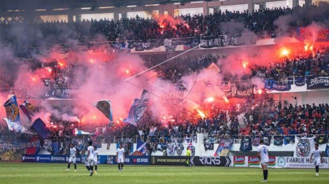 Sejumlah suporter Arema FC menyalakan suar atau flare seusai tim yang mereka dukung mencetak gol ke gawang PSIS Semarang pada laga uji coba di Stadion Jatidiri Semarang, Jawa Tengah, Sabtu (4/6/2022). (ANTARA FOTO/Aji Styawan/aww.)