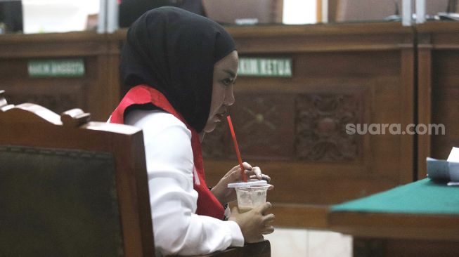 Medina Zein berhijab hitam seraya menyeruput minuman saat menjalani sidang di Pengadilan Negeri Jakarta Selatan, Senin (5/9). [Suara.com/Oke Atmaja]