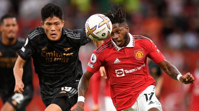 Gelandang Manchester United Fred (kanan) bersaing dengan bek Arsenal Takehiro Tomiyasu (kiri) saat pertandingan sepak bola Liga Premier Inggris antara Manchester United dan Arsenal di Stadion Old Trafford, Manchester, Inggris, Minggu (4/9/2022). [Oli SCARFF / AFP]