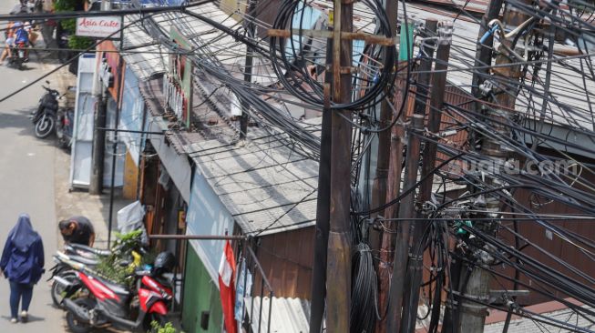 Deretan instalasi kabel yang semrawut di Kramat Jati, Jakarta Timur, Selasa (6/9/2022). [Suara.com/Alfian Winanto]