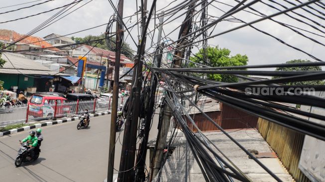 Deretan instalasi kabel yang semrawut di Kramat Jati, Jakarta Timur, Selasa (6/9/2022). [Suara.com/Alfian Winanto]