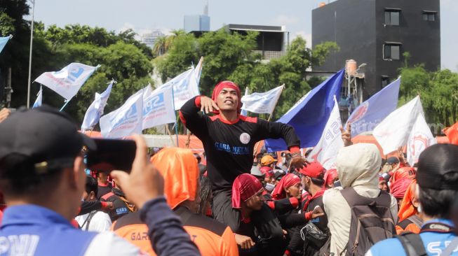 Massa Buruh saat menggelar aksi unjuk rasa di depan Gedung DPR RI, Senayan, Jakarta Pusat, Selasa (6/9/2022). Ada dari mereka yang joget dangan digendong. [Suara.com/Alfian Winanto]