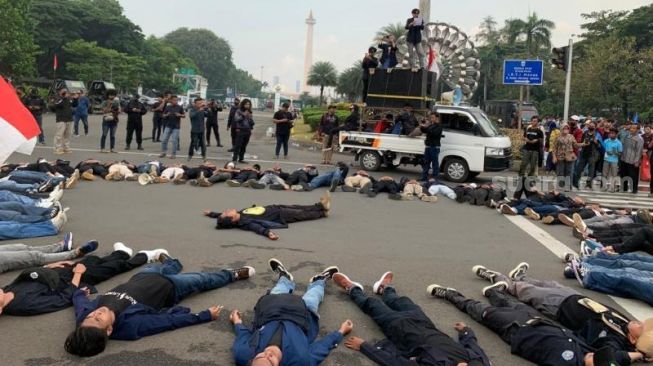 Massa mahasiswa yang melakukan demo tolak harga BBM naik melakukan aksi teaterikal dengan tidur di jalan di kawasan Silang Monas, Jakarta Pusat, Rabu (7/9/2022). [Suara.com/Rakha Arlyanto]