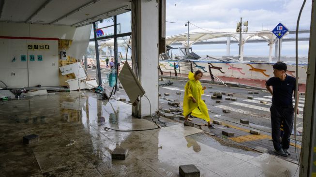 Pejalan kaki melewati deretan toko yang rusak parah akibat Topan Hinnamnor di Busan, Korea Selatan, Selasa (6/9/2022). [Anthony WALLACE/AFP]