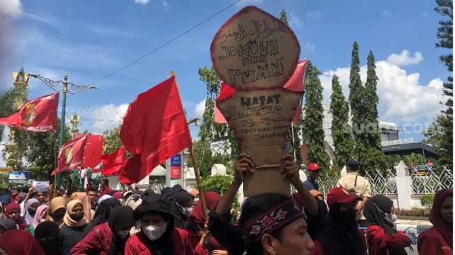 Mahasiswa saat membawa batu karton mirip batu nisan ke depan kantor DPRD NTB, Kamis (8/9/2022) (Suara.com/Toni Hermawan)