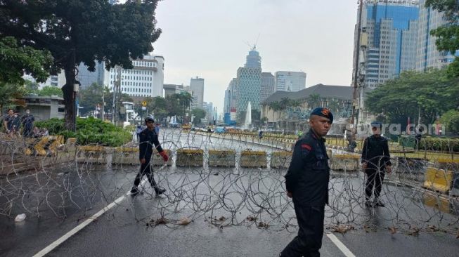 Pasukan Brimob saat memasang dua lapis kawat berduri jelang aksi tolak kenaikan BBM yang digelar massa BEM SI di Patung Kuda, Jakarta. (Suara.com/Yaumal)