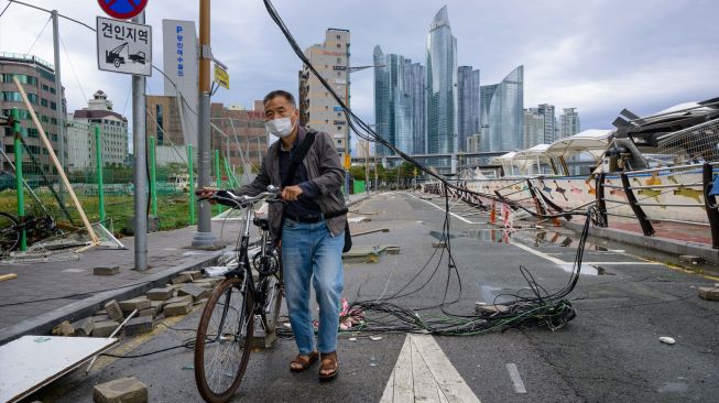  Seorang pria mendorong sepedanya di bawah kabel listrik yang rusak di jalan akibat Topan Hinnamnor di Busan, Korea Selatan, Selasa (6/9/2022). [Anthony WALLACE/AFP]
