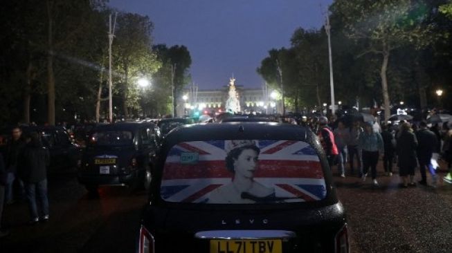 London taksi yang legendaris dengan potret Sri Ratu Elizabeth II di kaca belakang bergerak ke arah The Mall, bergabung dengan massa di luar gerbang Istana Buckingham, London setelah pengumuman mangkatnya Yang Mulia Ratu Elizabeth II (8/9/2022) [AFP/Isabel Infantes]