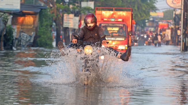 Tips naik motor di musim hujan antara lain mengulas soal pentingnya cara mengerem yang benar. Foto: Pengendara motor menerobos banjir yang merendam Jalan KH Hasyim Ashari dan Perumahan Ciledug Indah, Ciledug, Tangerang, Banten, Minggu (11/9/2022). [ANTARA FOTO/Muhammad Iqbal/YU]