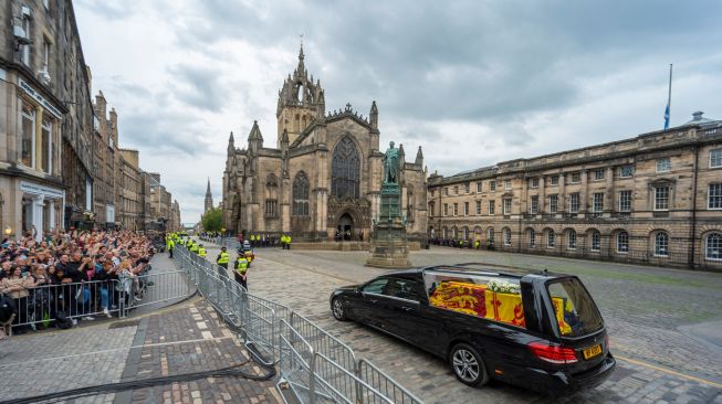 Mobil jenazah yang membawa peti mati Ratu Elizabeth II melintas di depan Katedral St Giles dalam perjalanan menuju Istana Holyroodhouse, Edinburgh, Skotlandia, Minggu (11/9/2022). [Andrew O'Brien / POOL / AFP]