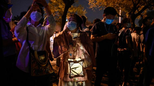 Seorang wanita dalam kostum tradisional memegang lentera saat Festival Pertengahan Musim Gugur di Beijing, China, Sabtu (10/9/2022). [Jade Gao / AFP]